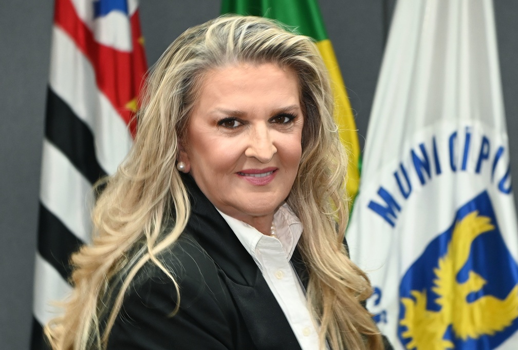 Secretária Adriana Flosi, de pé, com bandeiras do estado de São Paulo, do Brasil e de Campinas ao fundo