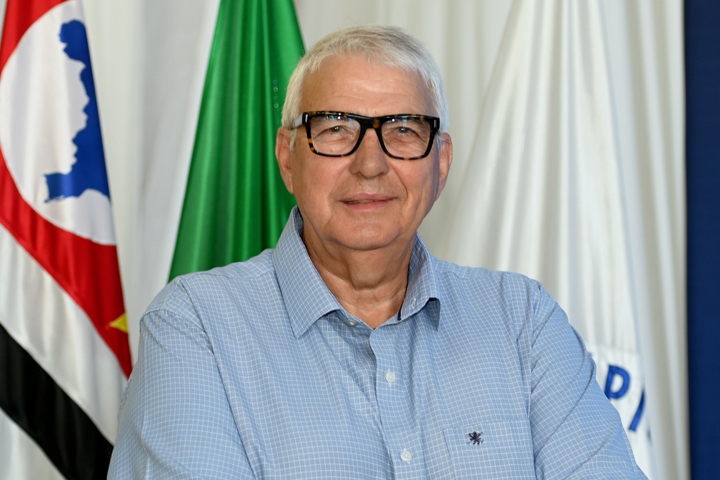 Fotografia do secretário Ernesto Dimas Paulella, com bandeiras ao fundo