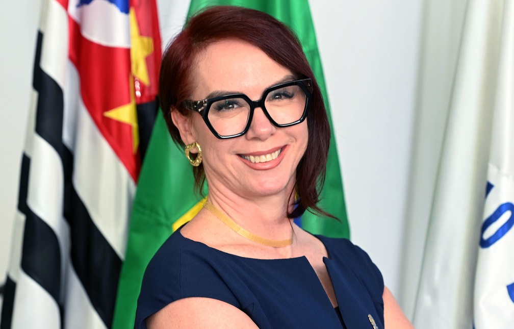 Fotografia da secretária Rose Guglielminetti, de pé e braços cruzados, com as bandeiras de Campinas, do Estado de São Paulo e do Brasil ao fundo