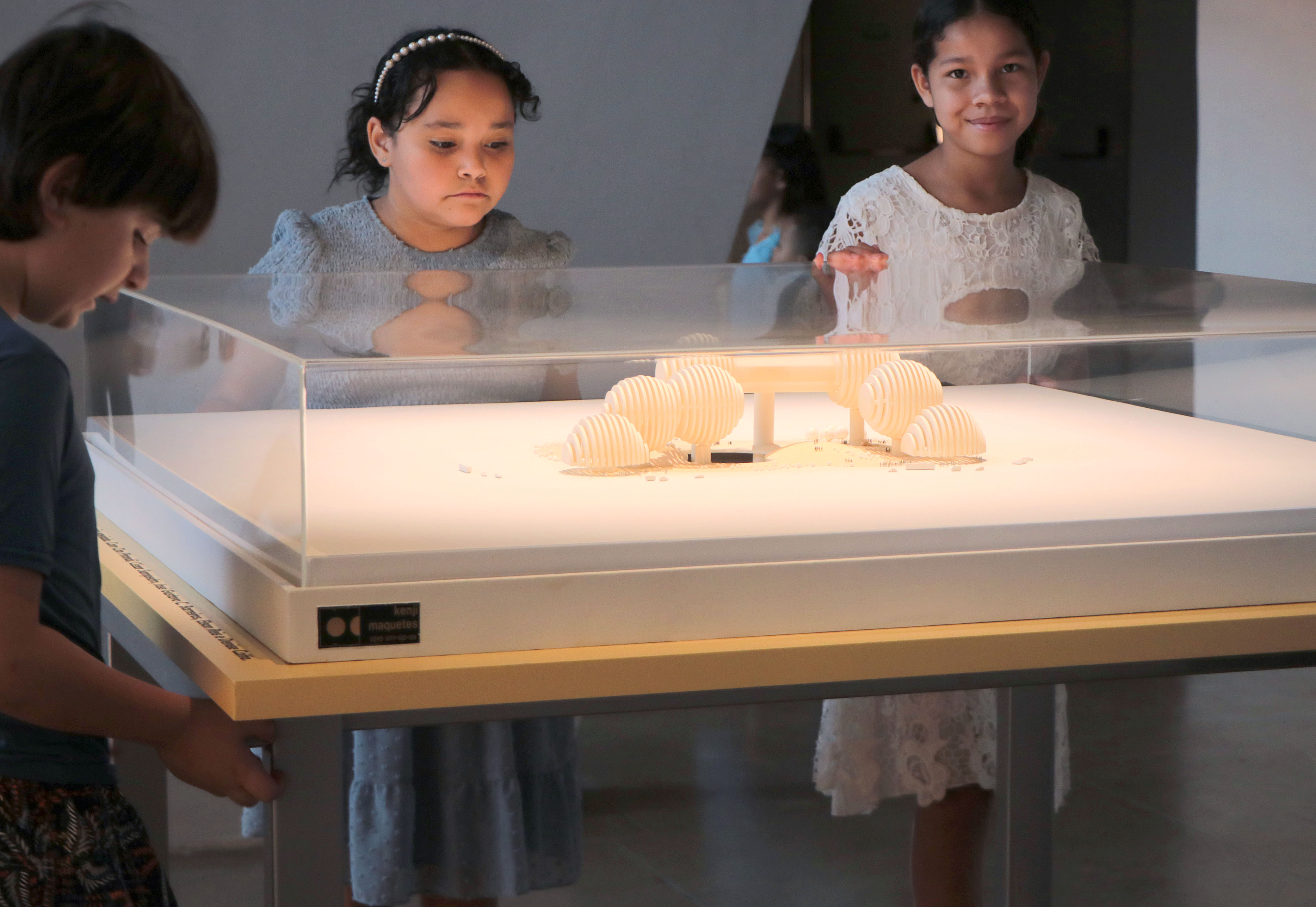 Crianças observam maquete arquitetônica que integra a exposição “Fábio Penteado: Pétalas e Estrelas”, evidenciando a proposta educativa e intergeracional da mostra