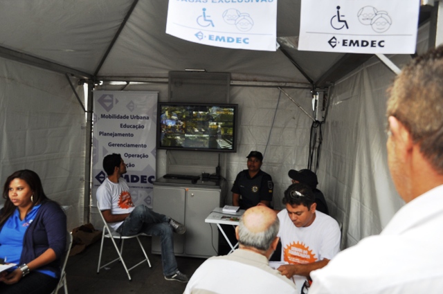 Pessoas sendo atendidas em estande da Emdec