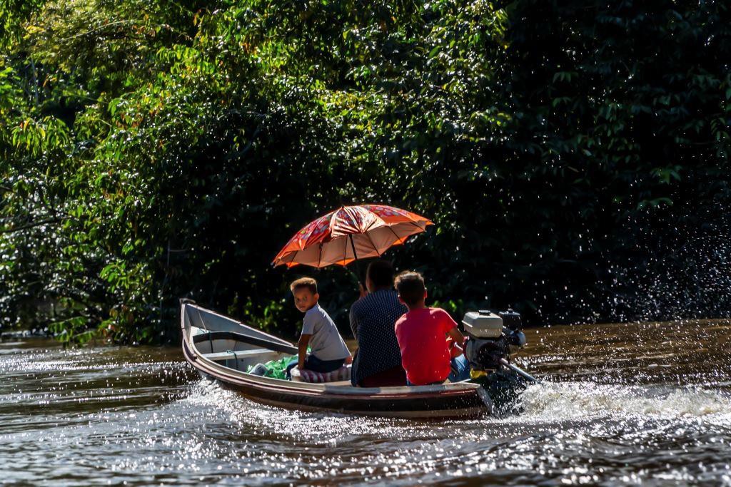 Protegida do sol por um guarda-chuva, família se desloca de canoa motorizada por rio da Amazônia acreana; para os povos da floresta, os rios funcionam como estradas 