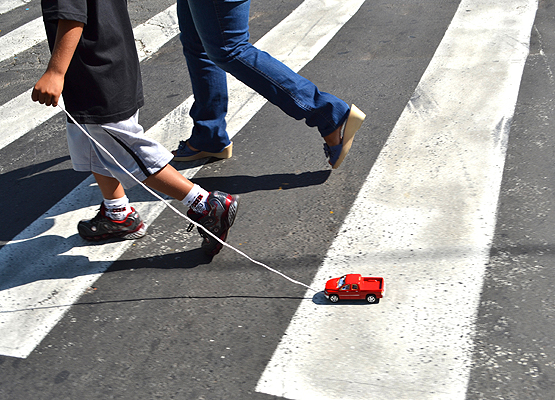 Foto de criança atravessando a rua na faixa de pedestre e puxa um carrinho de brinquedo