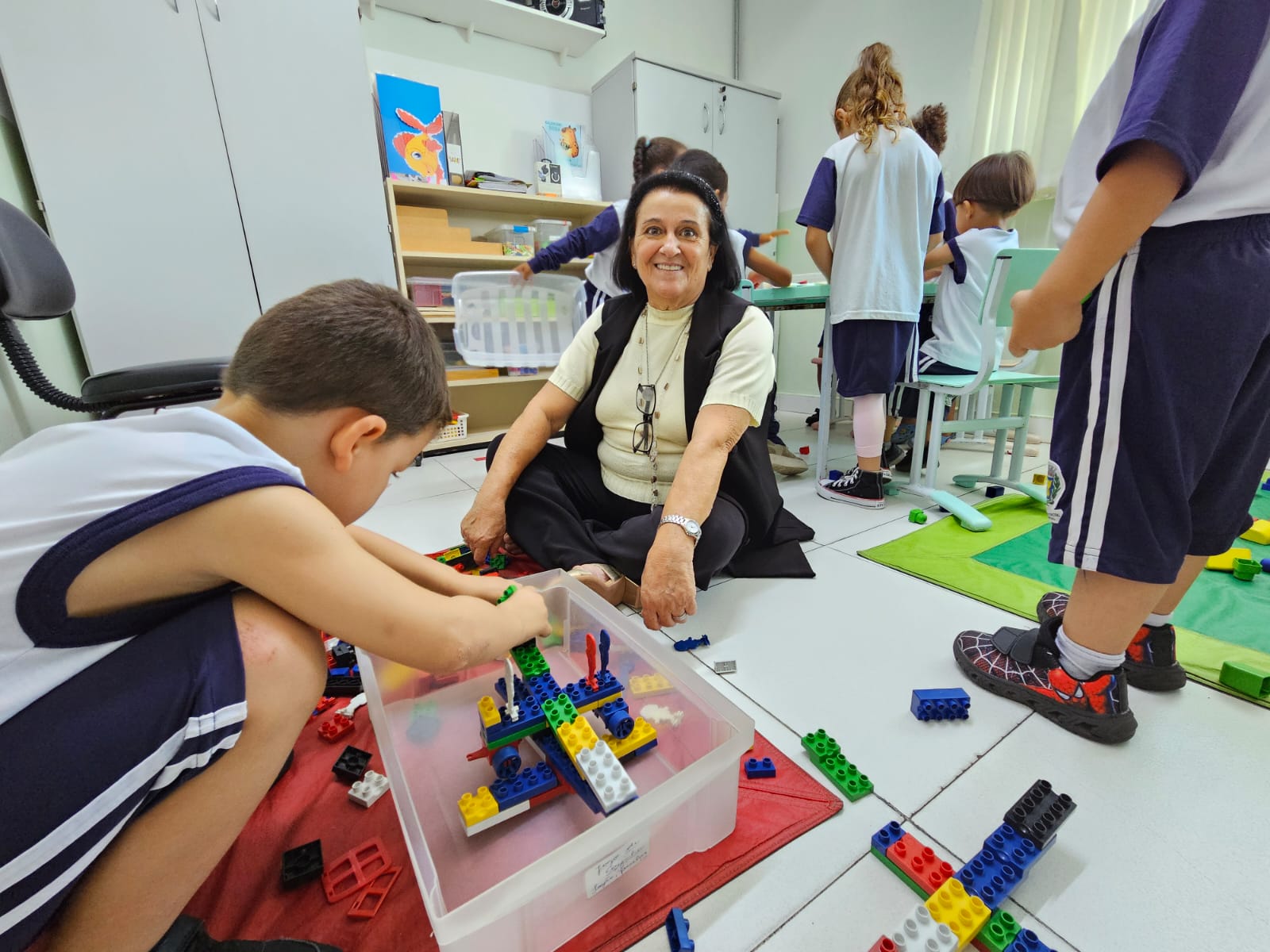 Imagem mostra a professora Ana Maria da Silveira Rogel Bueno interagindo com alunos da CEI Mauro Marcondes
